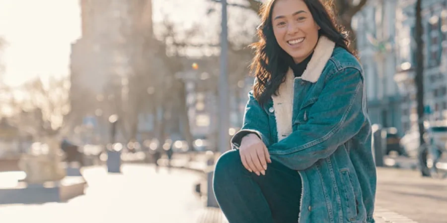 Girl sitting on a wall in a city park on a sunny day smiling at the camera.jpg